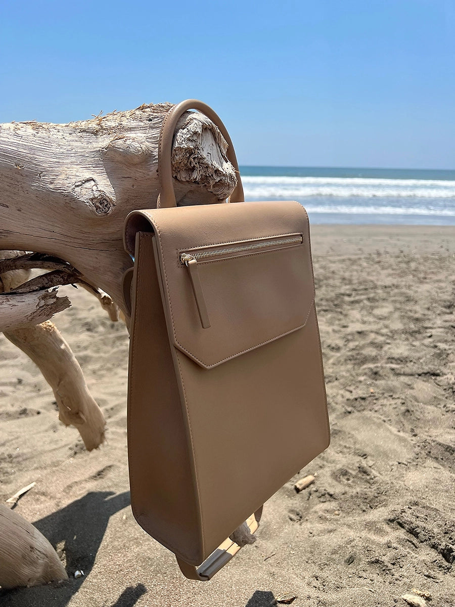 Tan Designer Handbag sitting on driftwood at the beach. Lo Zaino convertible backpack by Chandra Keyser