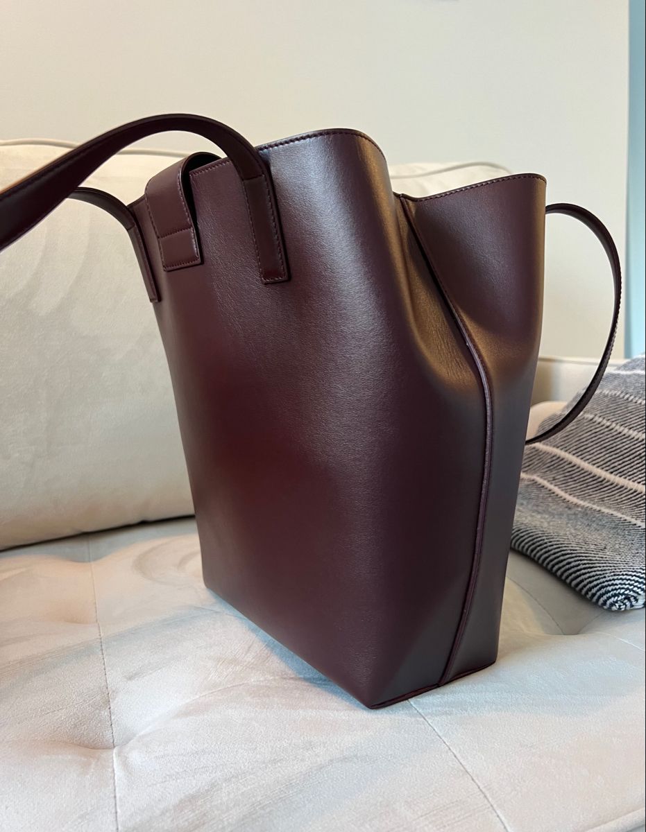 Bordeaux Red Leather tote sitting on creme velvet couch, La Borsa Structured Tote. Quiet Luxury style handbag made with smooth matte leather, by Chandra Keyser