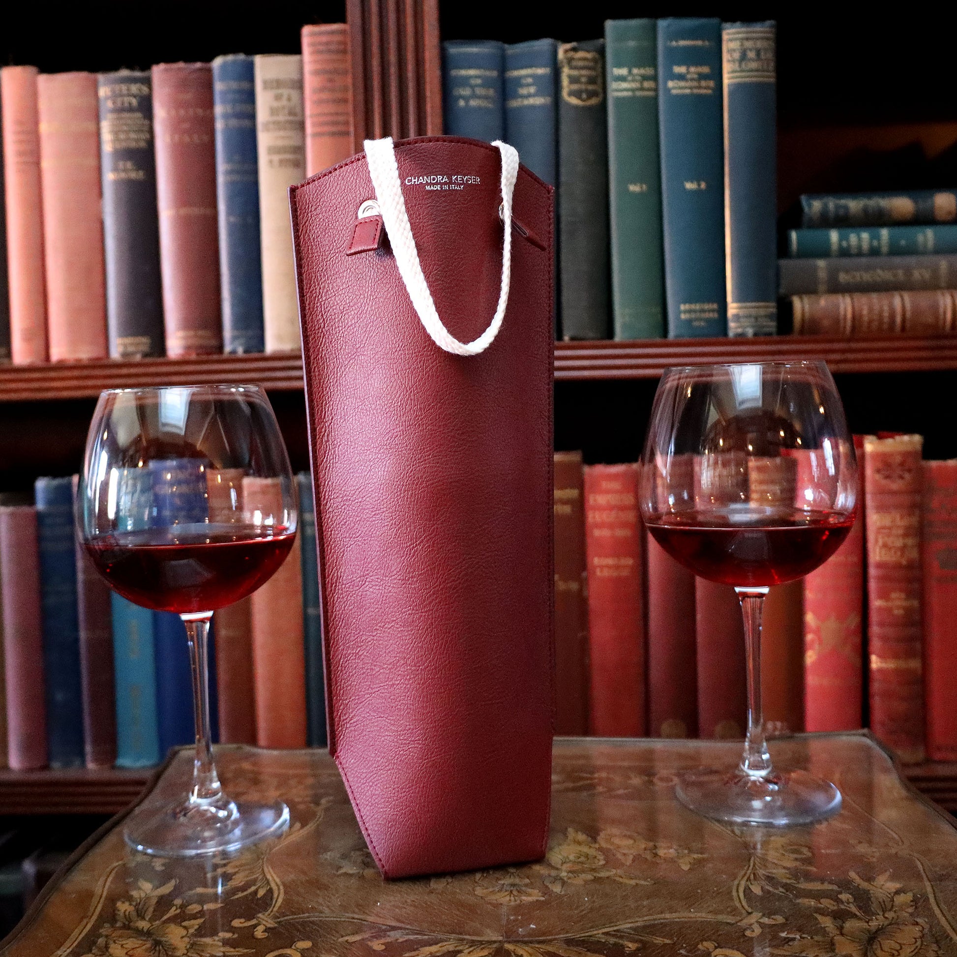 Sustainable Luxury Gift. Vegan Leather Wine Bag CHANDRA KEYSER La Borsa Da Vino Vegan Leather Wine Bag, on a side table with wine glasses and books.