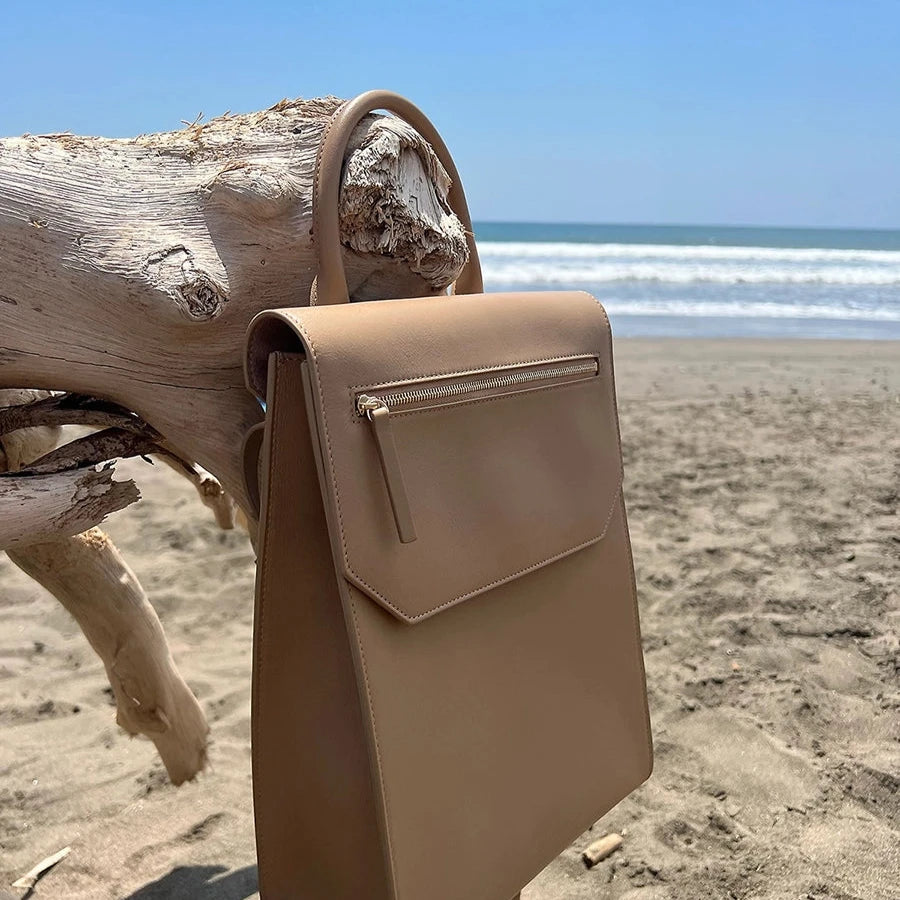 Tan Designer Handbag sitting on driftwood at the beach. Lo Zaino convertible backpack by Chandra Keyser