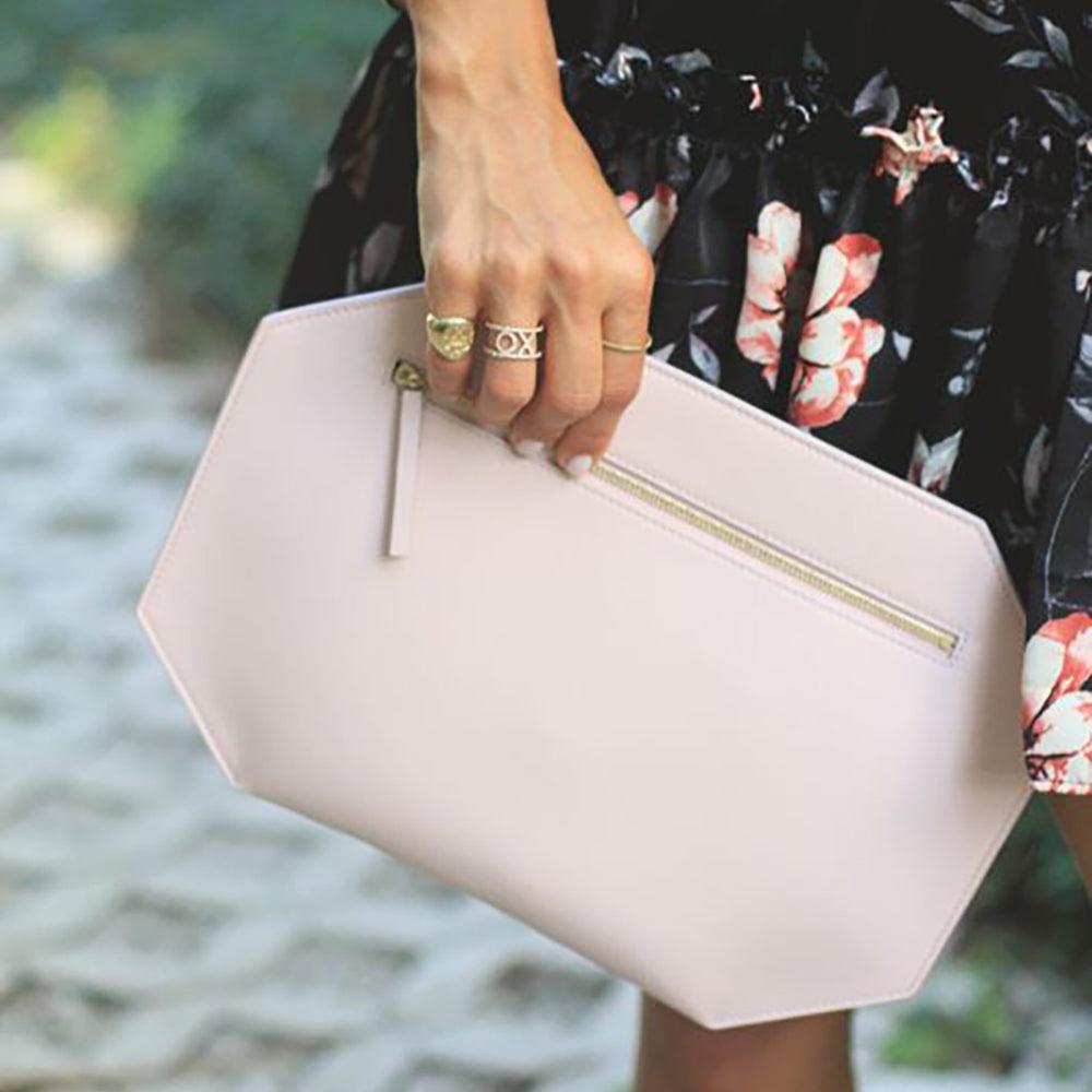 Pink smooth matte leather clutch, complementing black and pink flowered dress accessorized with gold jewelry. minimalist clutch quiet luxury Firenze clutch by Chandra Keyser