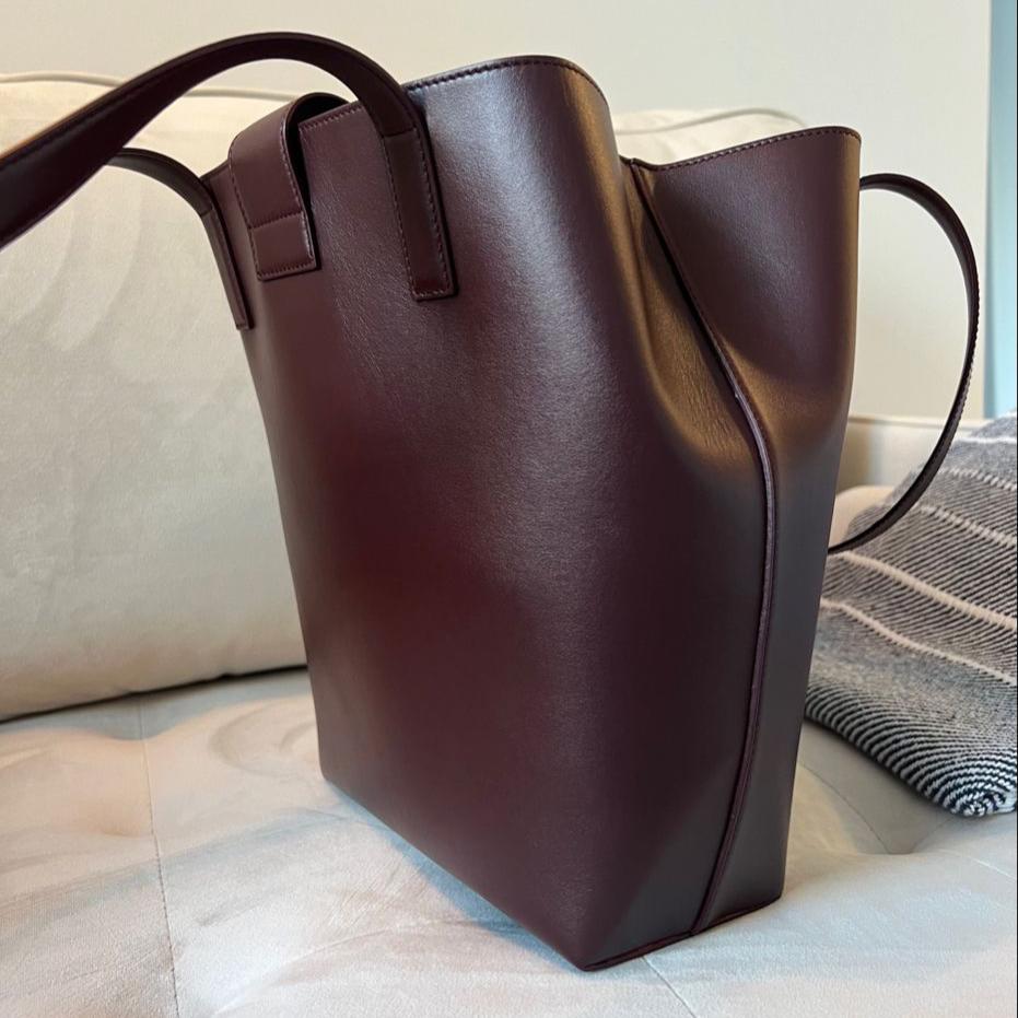 Bordeaux Red Leather tote sitting on creme velvet couch, La Borsa Structured Tote. Quiet Luxury style handbag made with smooth matte leather, by Chandra Keyser