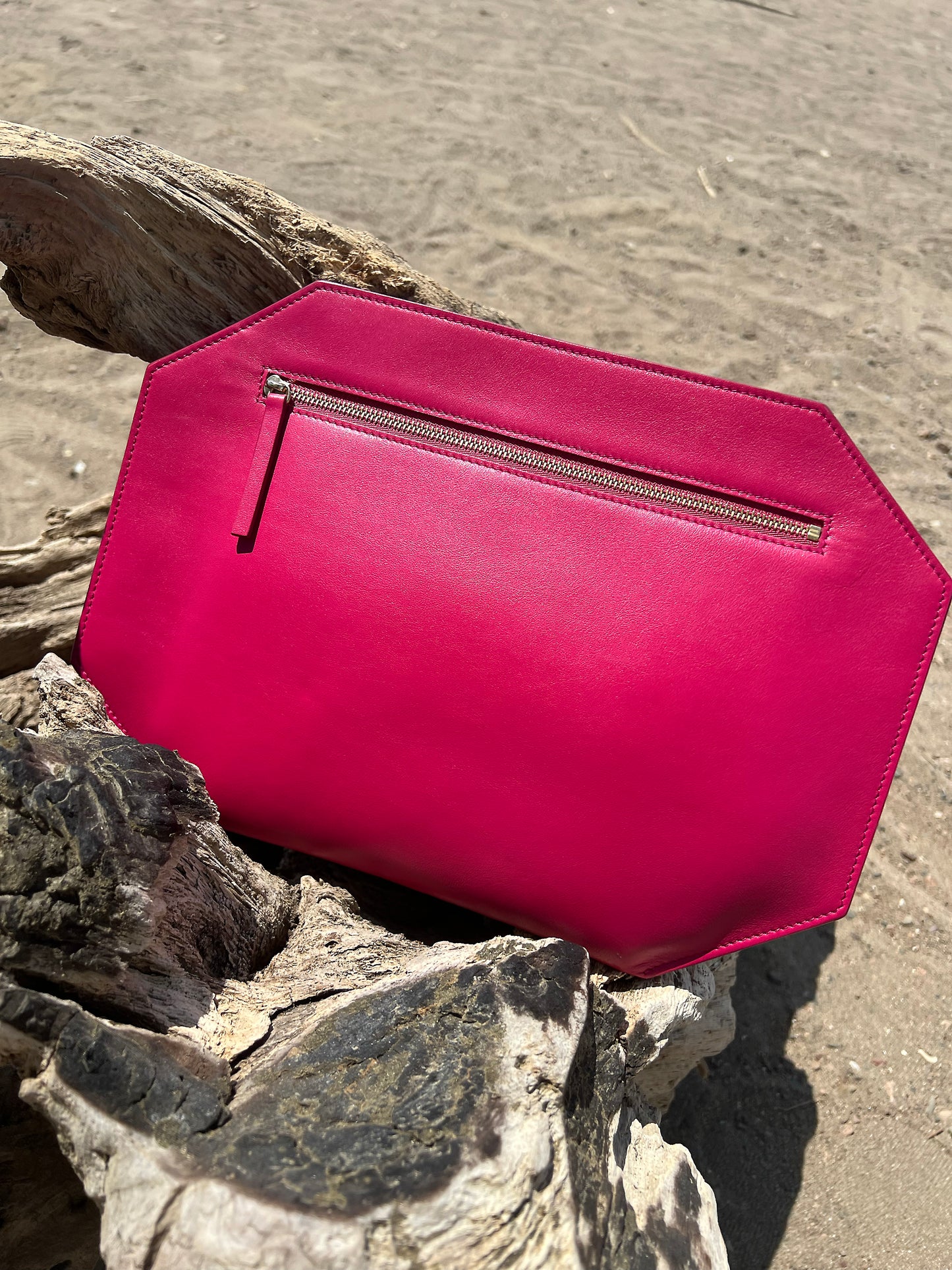sitting on driftwood at the beach. Pink smooth matte leather, Large zipper clutch in bright pink by Chandra Keyser