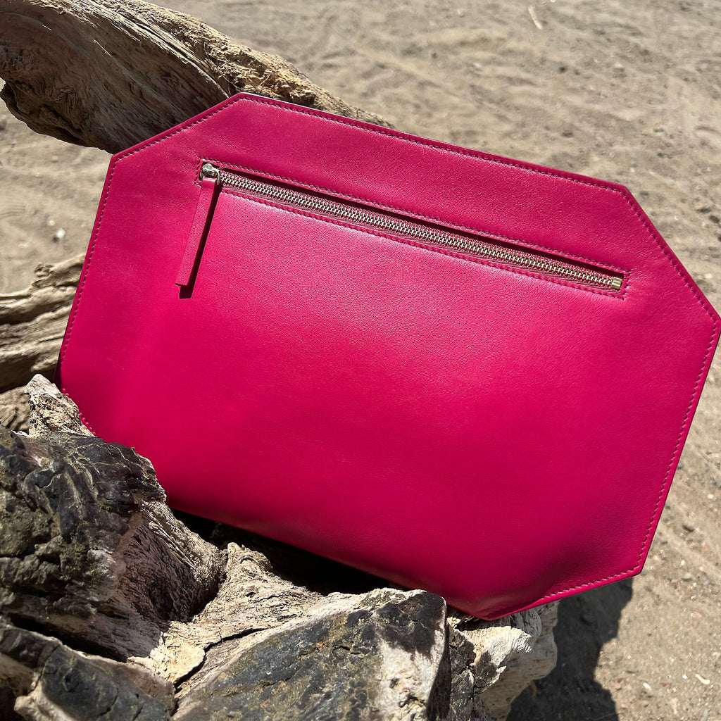 sitting on driftwood at the beach. Pink smooth matte leather, Large zipper clutch in bright pink by Chandra Keyser